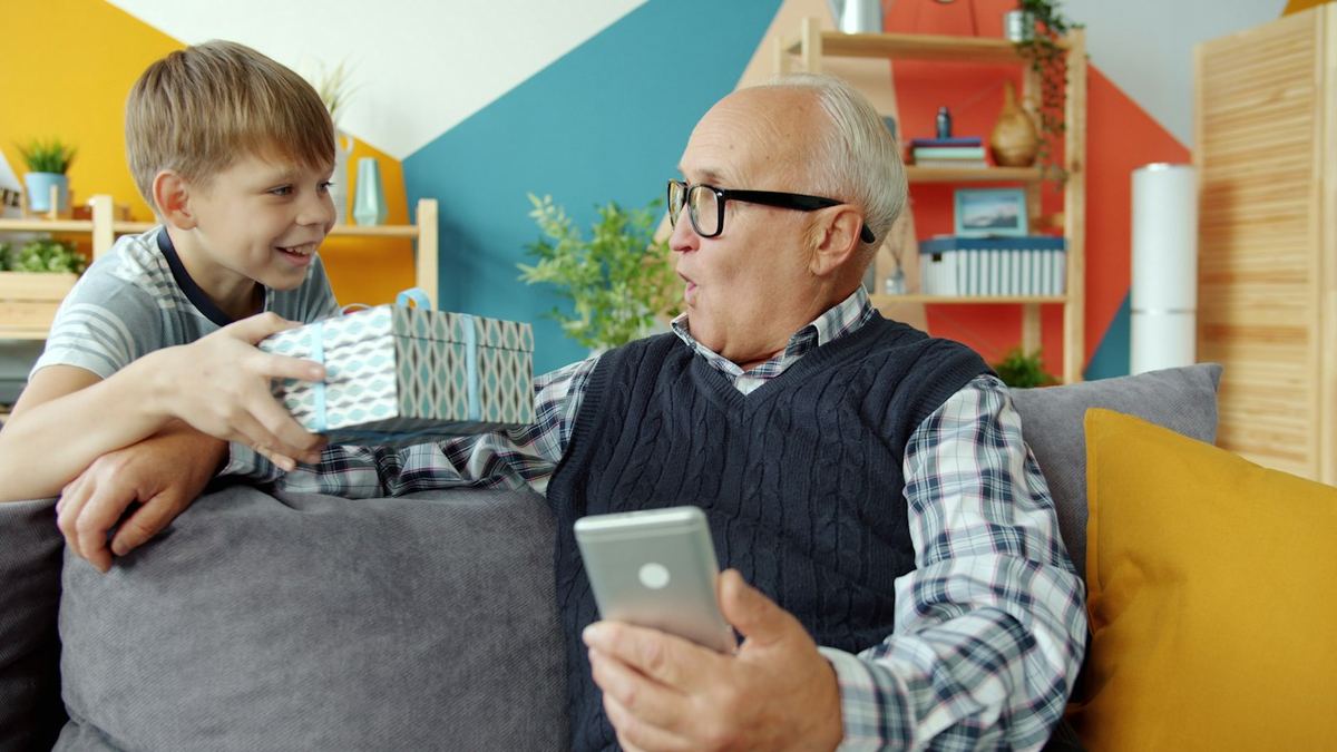 Two smiling grandparents receiving a gift from their grandson